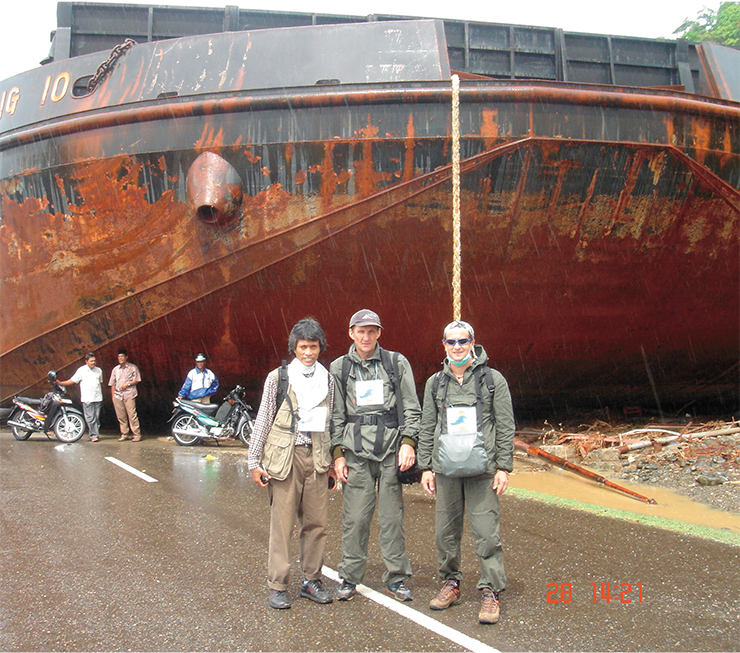Члены экспедиции (автор в центре) по изучению последствий Индонезийского цунами 26 декабря 2004 г. на фоне баржи с 5 тыс. тонн угля, перенесенной волной цунами через пирс на шоссе. Суматра, январь 2005 г. Фото автора