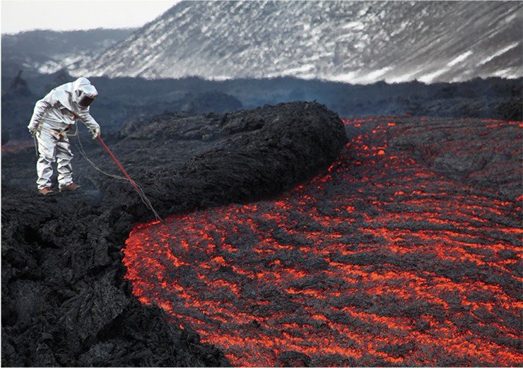 A volcanologist in an insulating suit measuring the temperature of the lava in a stream emerging from a lava duct in 1 kilometer from the active cinder cone of Tolbachik. March 2013. Photo by A. Belousov