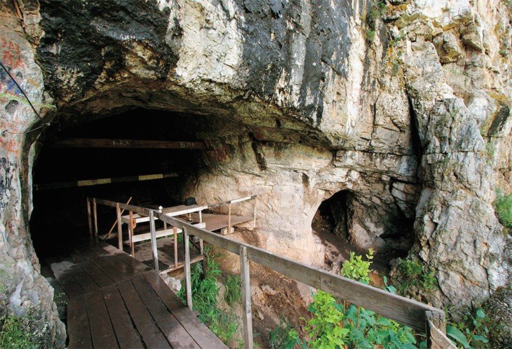 Денисова пещера – древнейшая обитаемая пещера в Северной Азии. Сегодня высота входа в пещеру составляет 6 м, а когда-то она была втрое меньше и тропа подходила под самое основание хребта (фото внизу). Нависший над входом потрескавшийся козырек в целях безопасности был обрушен точечными взрывами, на предвходовой площадке проведены раскопки, а вход в пещеру оборудован деревянным настилом (фото вверху). Фото С. Зеленского и из архива ИАЭТ СО РАН (1983)