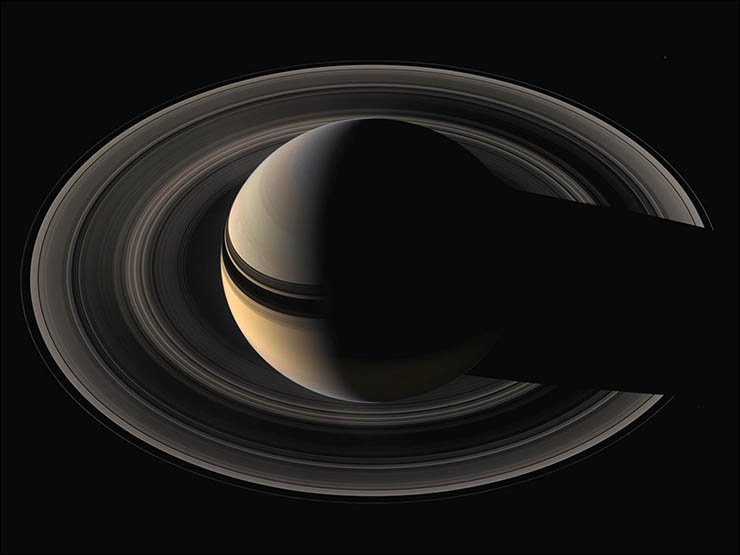 На этом снимке особенно хорошо видна тень кольца на облачной поверхности Сатурна и, разумеется, тень самой планеты на кольце. В данном случае мы видим ночную сторону кольца, недоступную для наблюдения с Земли