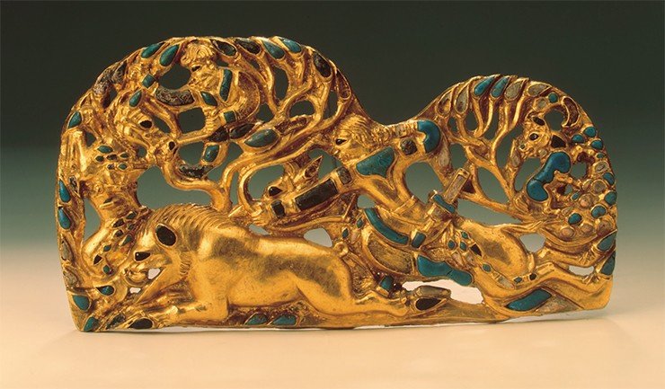 Одна из пары золотых поясных блях с изображением охоты всадника на кабана. Украшена вставками из синего непрозрачного стекла и коралла. III—II вв. до н. э. 